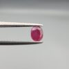 ​A 0.72-carat natural red Ruby (Yaqoot) from Kabul, Afghanistan, featuring an oval cut with a distinct yellow mountain inclusion on the back and a fine natural crack line on the front, held in jeweler's tweezers.