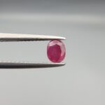 ​A 0.72-carat natural red Ruby (Yaqoot) from Kabul, Afghanistan, featuring an oval cut with a distinct yellow mountain inclusion on the back and a fine natural crack line on the front, held in jeweler's tweezers.