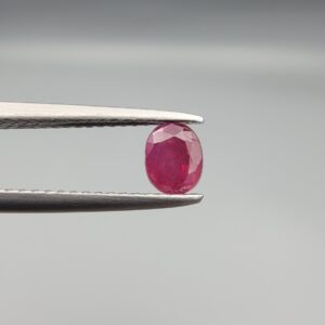 ​A 0.72-carat natural red Ruby (Yaqoot) from Kabul, Afghanistan, featuring an oval cut with a distinct yellow mountain inclusion on the back and a fine natural crack line on the front, held in jeweler's tweezers.