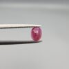 ​A 0.72-carat natural red Ruby (Yaqoot) from Kabul, Afghanistan, featuring an oval cut with a distinct yellow mountain inclusion on the back and a fine natural crack line on the front, held in jeweler's tweezers.