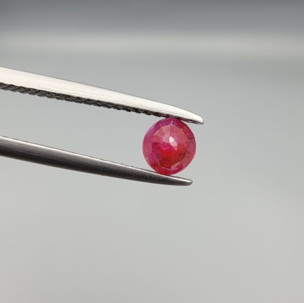 A 0.53-carat natural red Ruby (Yaqoot) from Kabul, Afghanistan, featuring a round brilliant cut with a unique yellow mountain inclusion on the back side, held in jeweler's tweezers.