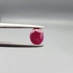 ​A 0.51-carat natural red Ruby (Yaqoot) from Kabul, Afghanistan, featuring an oval faceted cut with a distinct black mountain inclusion on the back side, held in jeweler's tweezers.