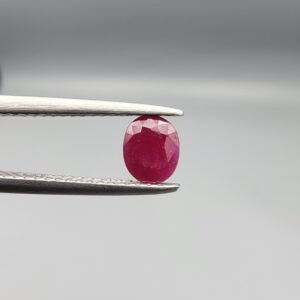 ​A 0.51-carat natural red Ruby (Yaqoot) from Kabul, Afghanistan, featuring an oval faceted cut with a distinct black mountain inclusion on the back side, held in jeweler's tweezers.