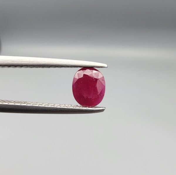 ​A 0.51-carat natural red Ruby (Yaqoot) from Kabul, Afghanistan, featuring an oval faceted cut with a distinct black mountain inclusion on the back side, held in jeweler's tweezers.