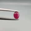 ​A 0.45-carat natural red Ruby (Yaqoot) from Kabul, Afghanistan, featuring an oval faceted cut with visible black mountain mineral inclusions on both the front and reverse sides, held in jeweler's tweezers.