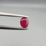 ​A 0.45-carat natural red Ruby (Yaqoot) from Kabul, Afghanistan, featuring an oval faceted cut with visible black mountain mineral inclusions on both the front and reverse sides, held in jeweler's tweezers.