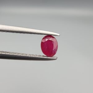 ​A 0.45-carat natural red Ruby (Yaqoot) from Kabul, Afghanistan, featuring an oval faceted cut with visible black mountain mineral inclusions on both the front and reverse sides, held in jeweler's tweezers.