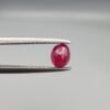 ​A 0.45-carat natural red Ruby (Yaqoot) from Kabul, Afghanistan, featuring an oval faceted cut with visible black mountain mineral inclusions on both the front and reverse sides, held in jeweler's tweezers.