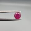 ​A 0.62-carat natural red Ruby (Yaqoot) from Kabul, Afghanistan, featuring a round cut with a natural black mountain inclusion on the back and tiny organic holes on the front, held in jeweler's tweezers.