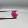 ​A 0.62-carat natural red Ruby (Yaqoot) from Kabul, Afghanistan, featuring a round cut with a natural black mountain inclusion on the back and tiny organic holes on the front, held in jeweler's tweezers.