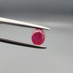 ​A 0.57-carat natural red Ruby (Yaqoot) from Kabul, Afghanistan, featuring an oval faceted cut with saturated red color and natural organic inclusions, held in jeweler's tweezers.