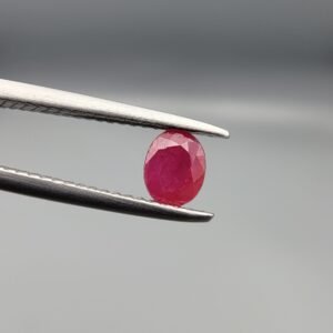 ​A 0.57-carat natural red Ruby (Yaqoot) from Kabul, Afghanistan, featuring an oval faceted cut with saturated red color and natural organic inclusions, held in jeweler's tweezers.