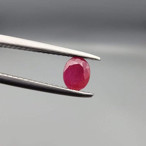 ​A 0.57-carat natural red Ruby (Yaqoot) from Kabul, Afghanistan, featuring an oval faceted cut with saturated red color and natural organic inclusions, held in jeweler's tweezers.