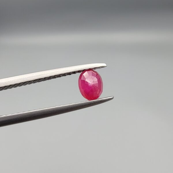 ​A 0.57-carat natural red Ruby (Yaqoot) from Kabul, Afghanistan, featuring an oval faceted cut with saturated red color and natural organic inclusions, held in jeweler's tweezers.
