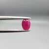 A 0.53-carat natural red Ruby (Yaqoot) from Kabul, Afghanistan, featuring an oval faceted cut with deep red saturation and natural earth-mined inclusions, held in jeweler's tweezers.