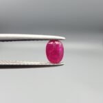 A 0.53-carat natural red Ruby (Yaqoot) from Kabul, Afghanistan, featuring an oval faceted cut with deep red saturation and natural earth-mined inclusions, held in jeweler's tweezers.