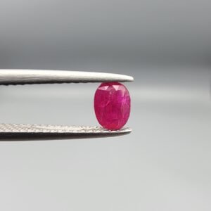 A 0.53-carat natural red Ruby (Yaqoot) from Kabul, Afghanistan, featuring an oval faceted cut with deep red saturation and natural earth-mined inclusions, held in jeweler's tweezers.