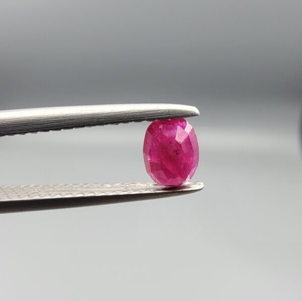 A 0.53-carat natural red Ruby (Yaqoot) from Kabul, Afghanistan, featuring an oval faceted cut with deep red saturation and natural earth-mined inclusions, held in jeweler's tweezers.