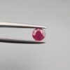 A 0.39-carat natural red Ruby (Yaqoot) from Kabul, Afghanistan, featuring a round brilliant cut with a natural mountain hole on the back and a tiny black inclusion on the front, held in jeweler's tweezers.
