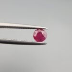 A 0.39-carat natural red Ruby (Yaqoot) from Kabul, Afghanistan, featuring a round brilliant cut with a natural mountain hole on the back and a tiny black inclusion on the front, held in jeweler's tweezers.