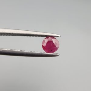 A 0.39-carat natural red Ruby (Yaqoot) from Kabul, Afghanistan, featuring a round brilliant cut with a natural mountain hole on the back and a tiny black inclusion on the front, held in jeweler's tweezers.