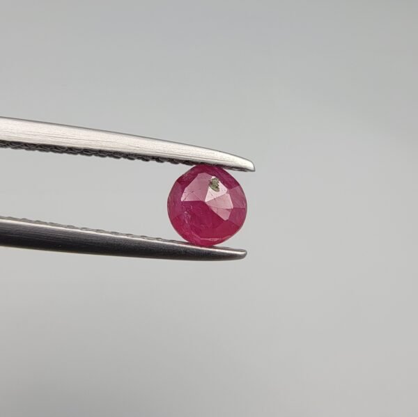 A 0.39-carat natural red Ruby (Yaqoot) from Kabul, Afghanistan, featuring a round brilliant cut with a natural mountain hole on the back and a tiny black inclusion on the front, held in jeweler's tweezers.