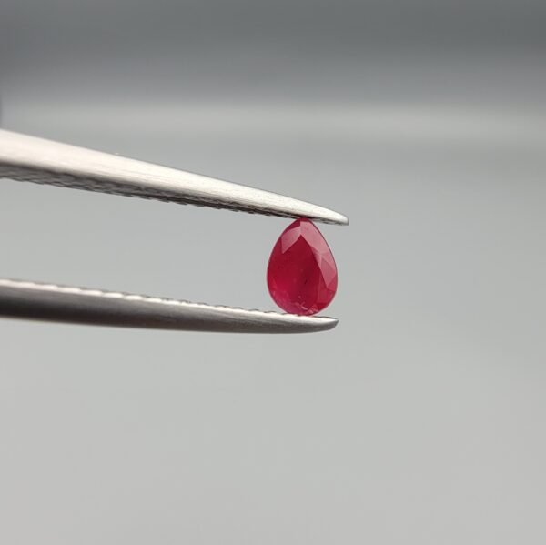A 0.44-carat natural red Ruby (Yaqoot) from Kabul, Afghanistan, featuring a brilliant pear faceted cut with rich red color and natural organic inclusions, held in jeweler's tweezers.