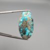 ​A large 45.87-carat natural Turquoise (Feroza) from Kerman, Iran, featuring a bold oval cabochon cut with a heavy golden pyrite matrix and deep blue-green color.