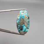 ​A large 45.87-carat natural Turquoise (Feroza) from Kerman, Iran, featuring a bold oval cabochon cut with a heavy golden pyrite matrix and deep blue-green color.