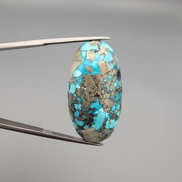 ​A large 45.87-carat natural Turquoise (Feroza) from Kerman, Iran, featuring a bold oval cabochon cut with a heavy golden pyrite matrix and deep blue-green color.