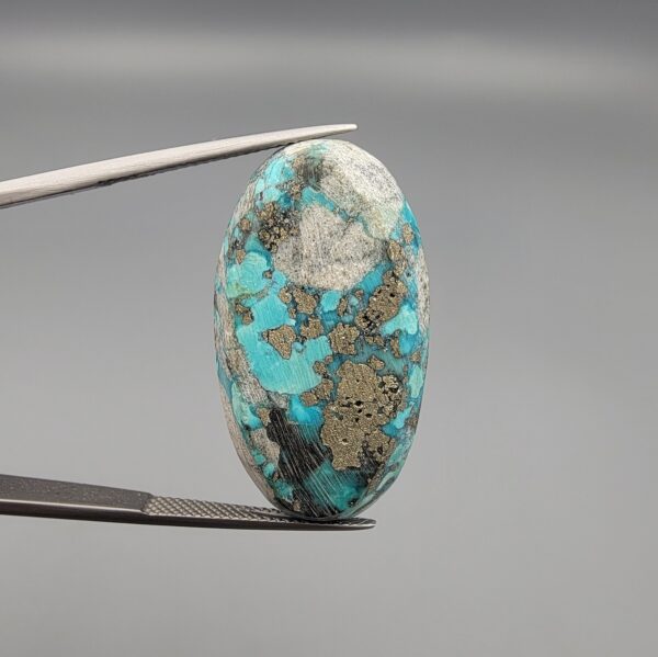 ​A large 45.87-carat natural Turquoise (Feroza) from Kerman, Iran, featuring a bold oval cabochon cut with a heavy golden pyrite matrix and deep blue-green color.