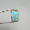 ​A 28.84-carat natural blue-green Turquoise (Feroza) from Kerman, Iran, featuring a unique rectangle cabochon cut with a shimmering golden pyrite matrix.