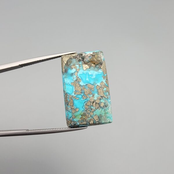 ​A 28.84-carat natural blue-green Turquoise (Feroza) from Kerman, Iran, featuring a unique rectangle cabochon cut with a shimmering golden pyrite matrix.