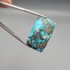 ​A 28.84-carat natural blue-green Turquoise (Feroza) from Kerman, Iran, featuring a unique rectangle cabochon cut with a shimmering golden pyrite matrix.