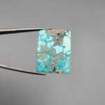 ​A 29.83-carat natural blue-green Turquoise (Feroza) from Kerman, Iran, featuring a unique rectangle cabochon cut with a shimmering golden pyrite matrix.