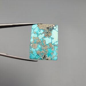 ​A 29.83-carat natural blue-green Turquoise (Feroza) from Kerman, Iran, featuring a unique rectangle cabochon cut with a shimmering golden pyrite matrix.