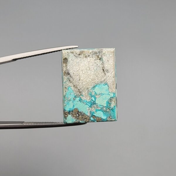 ​A 29.83-carat natural blue-green Turquoise (Feroza) from Kerman, Iran, featuring a unique rectangle cabochon cut with a shimmering golden pyrite matrix.