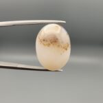 A 15-carat natural Milky Dendritic Agate (Shajari Aqeeq) from Iran, featuring a smooth oval cabochon cut with sharp black tree-like inclusions on a misty-white background.