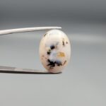 ​A 10-carat natural Milky Dendritic Agate (Shajari Aqeeq) from Iran, featuring an oval cabochon with sharp black and brown tree-like inclusions on the front and a clear, inclusion-free milky reverse side.