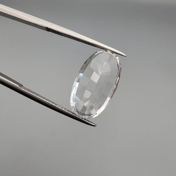 ​A large 14.78-carat natural Kunzite gemstone from Pakistan, featuring an oval faceted cut, eye-clean clarity, and a light pink to white color-shift effect, held in jeweler's tweezers.