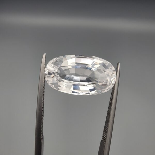 ​A large 14.78-carat natural Kunzite gemstone from Pakistan, featuring an oval faceted cut, eye-clean clarity, and a light pink to white color-shift effect, held in jeweler's tweezers.