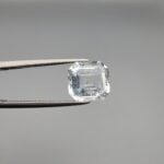 ​A 4-carat natural Shigar Valley Aquamarine (Beruj) gemstone with an octagon emerald cut, displaying a clear sea-blue color and unique natural inclusions, held in jeweler's tweezers.