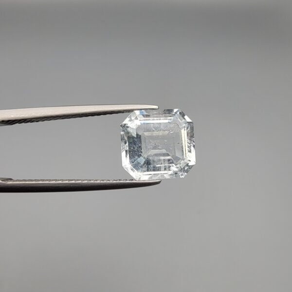 ​A 4-carat natural Shigar Valley Aquamarine (Beruj) gemstone with an octagon emerald cut, displaying a clear sea-blue color and unique natural inclusions, held in jeweler's tweezers.