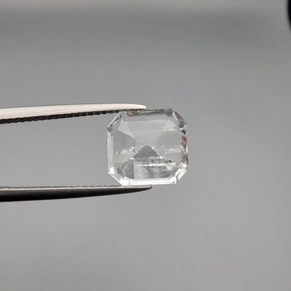 ​A 4-carat natural Shigar Valley Aquamarine (Beruj) gemstone with an octagon emerald cut, displaying a clear sea-blue color and unique natural inclusions, held in jeweler's tweezers.