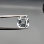 A 3.58-carat natural Shigar Valley Aquamarine (Beruj) gemstone with an octagon emerald cut, displaying a clear sea-blue hue and unique organic inclusions, held in jeweler's tweezers.