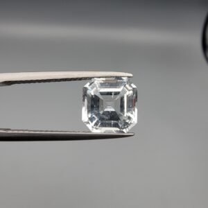 A 3.58-carat natural Shigar Valley Aquamarine (Beruj) gemstone with an octagon emerald cut, displaying a clear sea-blue hue and unique organic inclusions, held in jeweler's tweezers.