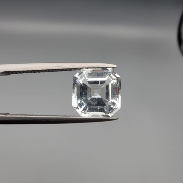 A 3.58-carat natural Shigar Valley Aquamarine (Beruj) gemstone with an octagon emerald cut, displaying a clear sea-blue hue and unique organic inclusions, held in jeweler's tweezers.