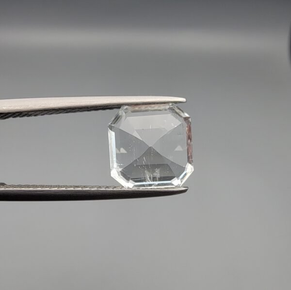 A 3.58-carat natural Shigar Valley Aquamarine (Beruj) gemstone with an octagon emerald cut, displaying a clear sea-blue hue and unique organic inclusions, held in jeweler's tweezers.