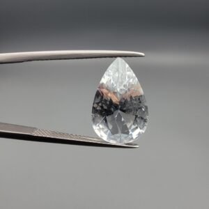 ​A large 5.35-carat natural Shigar Valley Aquamarine (Beruj) gemstone with a pear-shaped faceted cut, displaying an icy-blue color and organic mountain inclusions, held in jeweler's tweezers.