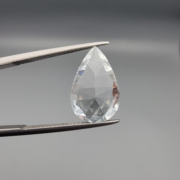 ​A large 5.35-carat natural Shigar Valley Aquamarine (Beruj) gemstone with a pear-shaped faceted cut, displaying an icy-blue color and organic mountain inclusions, held in jeweler's tweezers.